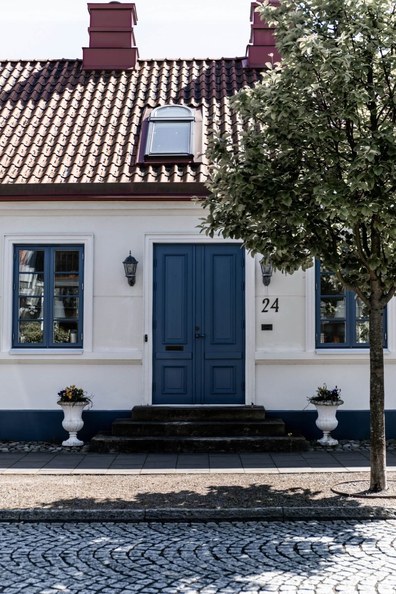 Detta hus utstrålar klass med sin vita putsade yta, dörr och fönster i blått, samt en trottoar av kullersten